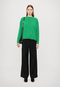 Green oversized sweater with ribbed neckline, paired with black wide-leg trousers and black pointed-toe ankle boots; minimalist design.