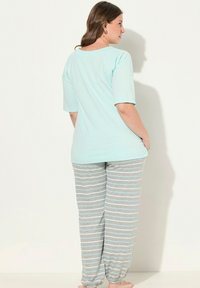 Světle modrý top s krátkým rukávem; šedé pruhované kalhoty s elastickými manžetami. Tkanina vypadá měkce a ležérně. Model stojí s rukama v kapsách.