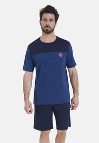 Chemise bleu marine à manches courtes avec des rayures horizontales bleues et un logo rond rouge ; associée à un short bleu marine, le tout en tissu doux.
