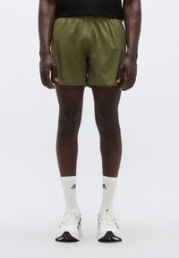 Πράσινο αθλητικό σορτς με ελαστική μέση, με αντίθετα λογότυπα, φορεμένο με λευκές κάλτσες πλήρους μήκους και παπούτσια τρεξίματος με μαύρες λεπτομέρειες.