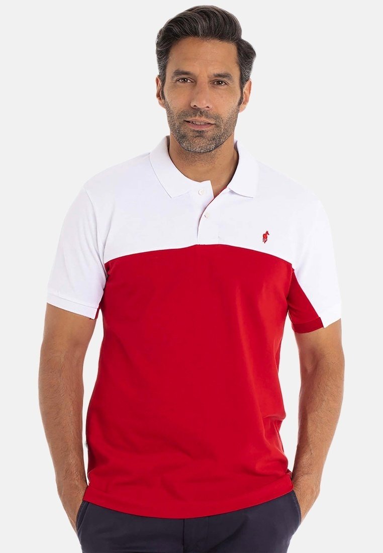 Homme portant un polo à manches courtes avec une partie supérieure blanche et une partie inférieure rouge, se tenant les mains dans les poches.