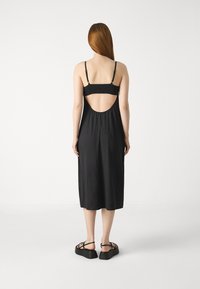 Musta midi-mekko ohuilla olkaimilla ja smockatulla selkäosalla. Mekossa on pyöreä aukko selän yläosassa, vaate laskeutuu kauniisti ja sen kangas on sileä.