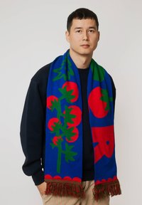 Dziany szalik z niebieskim tłem i wzorami zielonych i czerwonych pomidorów oraz liści. Ma frędzle na krawędziach.