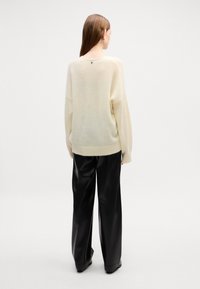 Maglione oversize crema con una texture morbida, orlo a costine e un sottile dettaglio a bottone sul retro, abbinato a pantaloni in pelle neri a vita alta.