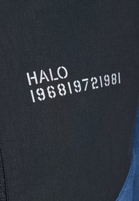 Schwarzer Stoff mit gerippter Textur zeigt das Wort "HALO" und die Zahlen "196819721981" in Weiß, auf der Oberfläche gedruckt.