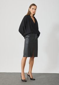 Μαύρη, φαρδιά μπλούζα με μακριά μανίκια και V λαιμόκοψη, συνδυασμένη με μια μαύρη δερμάτινη φούστα με ψηλή μέση και μπροστινό σκίσιμο. Μαύρα ψηλοτάκουνα παπούτσια.