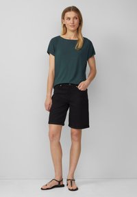Haut vert à manches courtes, short en denim noir avec ourlets retroussés, et sandales noires. Design simple, tissu léger et coupe décontractée.