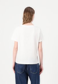 White short-sleeve T-shirt with a crew neckline, relaxed fit, and smooth texture. Paired with dark blue, loose-fitting denim jeans.