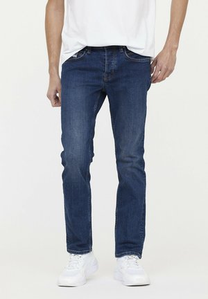 Donkerblauwe denim jeans met een rechte pasvorm, vijfzakontwerp, contrasterende stiksels en een ritssluiting. Gecombineerd met witte sneakers.
