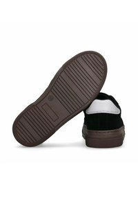 Sneaker in suede nero con un accento bianco sul tallone, suola in gomma marrone con un pattern di battistrada rigato e cuciture rinforzate lungo i bordi.