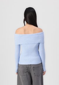Lysblå ribbet off-shoulder sweater med lange ærmer og tætsiddende talje. Struktureret stof giver en tætsiddende pasform. Bæres med grå vidde bukser.