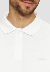 Weißes Polohemd aus strukturiertem Stoff; verfügt über eine Knopfleiste und ein kleines gesticktes Logo auf der Brust.