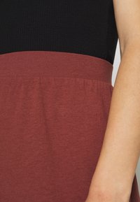 Haut noir côtelé avec une taille élastique bordeaux. Le tissu est lisse avec une légère brillance ; la taille présente des détails froncés pour un ajustement parfait.