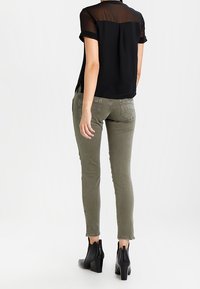 Černá blůza s krátkým rukávem z průsvitného materiálu a s ohrnutými manžetami, v kombinaci s olivově zelenými skinny džíny a černými koženými kotníkovými botami na podpatku.