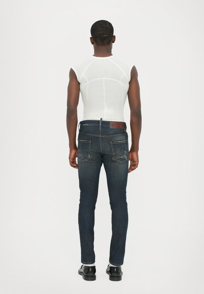 Short-sleeve white top and dark blue slim-fit jeans with subtle fade, featuring back pockets and a branded waistband. Smooth texture.