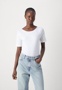 White short-sleeve t-shirt with a scoop neck, made of lightweight fabric. Paired with light blue relaxed-fit jeans, featuring a faded texture.