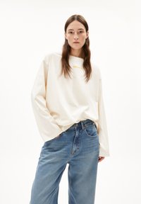 Crèmekleurig longsleeve-shirt met een ronde hals en gouden tekst. Draag het met lichtblauwe, hooggekropte, wijde jeans met voorzakken.