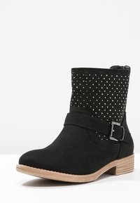 Czarne botki za kostkę z płaskim obcasem, wykonane z materiału przypominającego zamsz, z detalem klamry i ćwiekami na cholewie. Teksturalny, elegancki design.