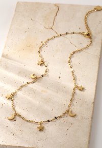 Collier en chaîne dorée présentant des charms alternés en forme de lune et d'étoile. Les maillons sont polis, créant une surface réfléchissante. Design minimaliste.
