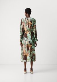 Abito trasparente con maniche lunghe, su sfondo marrone e vivaci motivi floreali in verde, arancione e blu. Presenta una vita arricciata e una silhouette fluida.
