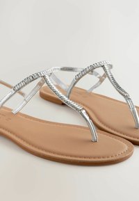 Zilveren metalen teensandalen met een gestructureerde band en een gladde tan voetbed, met een minimalistisch ontwerp en een slanke silhoët.