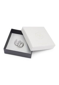 Silberne Creolen, die in einer schwarzen Box mit hellgrauem Innenfutter präsentiert werden. Die Box ist teilweise geöffnet und hat einen strukturierten weißen Deckel.