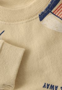 Felpa girocollo beige in cotone con collo e polsini a costine. Presenta un design stampato colorato sul davanti e una superficie morbida e texturizzata.