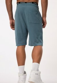 Teal katoenen shorts met een elastische tailleband en een zwart logo. Afgewerkt met een enkele achterzak. Gladde textuur en knielange snit.