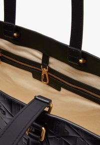 Sac à main noir texturé avec deux poignées, quincaillerie dorée et intérieur beige comportant une poche zippée.