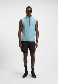 Light blue sleeveless top with a high collar and front zip, paired with black shorts and black sneakers with cream soles. Accented socks.