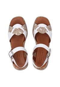 Weiße Sandalen mit einem geometrischen braunen Muster auf den Sohlen, verstellbaren Knöchelriemen und einer strukturierten Innensohle für mehr Komfort.