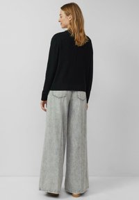 Czarny sweter z dzianiny w połączeniu z szerokimi szarymi dżinsami o luźnym kroju. Sweter ma prążkowany dół i subtelny szew z tyłu; spodnie mają wyblakłą fakturę.