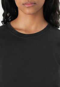 T-shirt en coton noir avec col rond, présentant une texture lisse et des manches courtes. Design simple, sans motifs ou logos visibles.