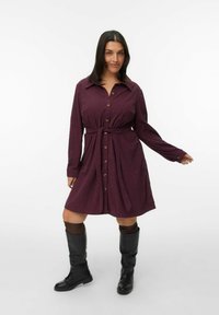 Bordeaux shirtjurk met een ceintuur in de taille, kraag en knoopsluiting; gemaakt van een gestructureerde stof. Zwarte kniehoge laarzen maken de outfit compleet.