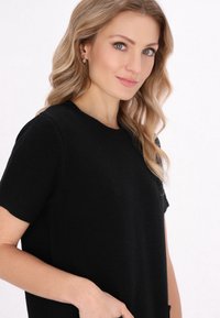 Pulover negru cu mânecă scurtă, din tricot texturat, cu gât rotund și croială lejeră. Materialul pare moale și confortabil.