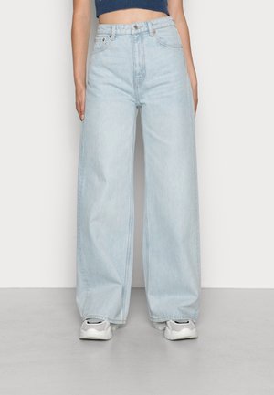 Ljust blå vida jeans i denim, med hög midja, sydda detaljer och en avslappnad passform, i kombination med vita och svarta sneakers.