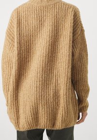 Pull en tricot marron clair avec une texture côtelée. Il possède un col haut, une coupe oversize et des épaules tombantes pour une silhouette décontractée.