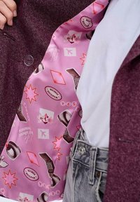Bordowy żakiet z różowym wzorzystym wykończeniem, na którym znajdują się różne grafiki, w tym kwiaty, gwiazdy i retro przedmioty, takie jak telefon.