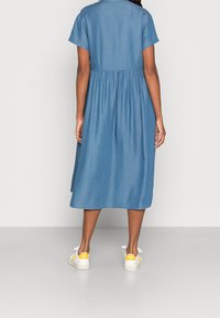 Džínsové šaty s krátkým rukávem a nařaseným pasem. Délka do půli lýtek, světle modré barvy. V kombinaci s bílými teniskami s žlutými akcenty.