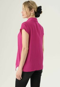 Camicetta corta rosa senza maniche con colletto, tessuto strutturato e spacchi laterali, abbinata a pantaloni neri aderenti. Design per una vestibilità rilassata.