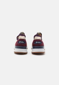 Vinröda och krämfärgade sneakers med en stickad krage, vit mellansula och brun gummisula, med en blå "Polo"-logotyp på baksidan.