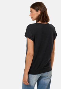 Top nero a maniche corte realizzato in tessuto morbido, con una vestibilità comoda e un colletto rotondo, abbinato a jeans di denim blu chiaro.