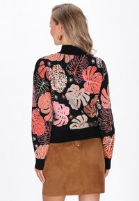 Fekete pulóver színes botanikai mintákkal pink, narancs és zöld színben, bordás mandzsettával és szegéllyel, bézs velúrbőrből készült szoknyával párosítva.