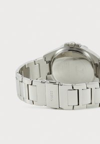 Montre en acier inoxydable argenté avec un bracelet poli. Boîtier rond et fond plat, avec une couronne et un nom de marque gravé sur le bracelet.