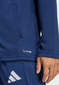 Ναυτικο μπλε αθλητική μπλούζα με λεία υφή, διαθέτει κρυφή τσέπη με φερμουάρ, σήμα CLIMACOOL και λευκή λεπτομέρεια με το λογότυπο της Adidas στο κάτω μέρος.