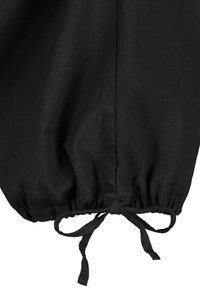 Schwarzes Stoffkleidungsstück mit einer gerafften Manschette und Zugbanddetail. Weiche Textur, glatte Oberfläche und minimal sichtbare Nähte.