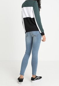 Färgglatt blockad sweatshirt i mörkgrön, vit och svart; ihop med ljusblå tighta jeans och svarta sneakers med vita sulor.