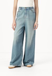 Jeans din denim albastru cu picioare largi și talie înaltă, având închidere cu nasture, ușoară decolorare și buzunare laterale. Textură moale și croială relaxată.
