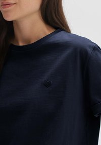 T-shirt di cotone blu navy con collo a girocollo, caratterizzato da un piccolo ricamo a forma di cuore nella zona sinistra del petto. Tessuto morbido.