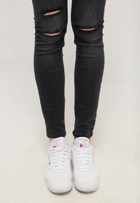 Vita sneakers med snören, med en texturerad ovandel och logotypdetalj. Ader med svarta skinny jeans med slitningar vid knäna.